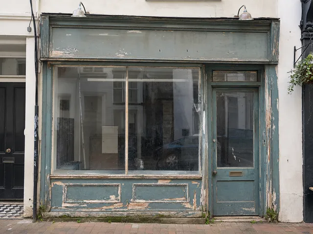 A shopfront with faded, flaking green paint and a weathered fascia.