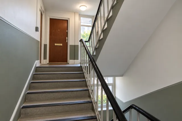 The same stairwell with fresh walls, a green-grey lower half and a black handrail.