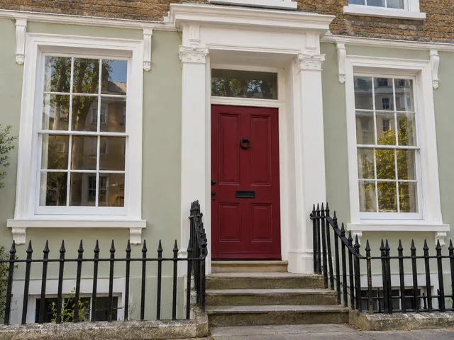 The same townhouse with restored white sash windows, pale green render and a red front door.