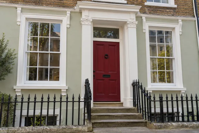 The same townhouse with restored white sash windows, pale green render and a red front door.