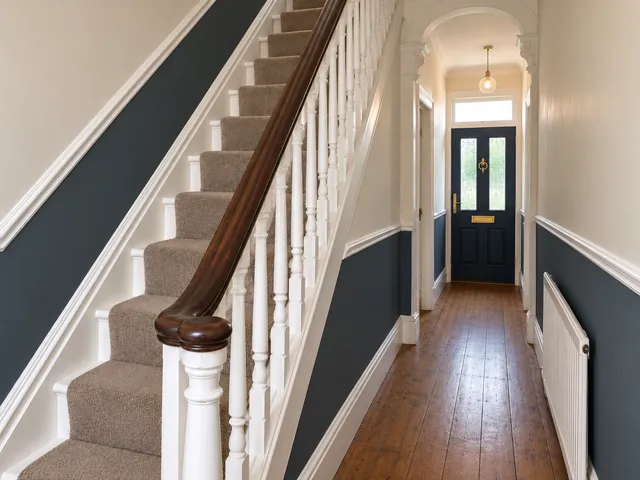 The same hallway with off-white walls, a navy lower half, white spindles and a navy front door.